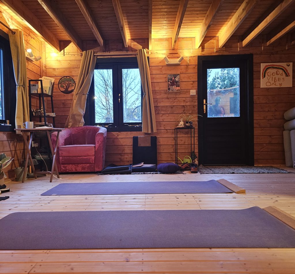A wooden beamed yoga studio with mats on the floor. Our studio(shed) is in Carisbrooke in Isle of Wight where Eva offers trauma informed Yoga  classes with Yoga Nidra for all sizes